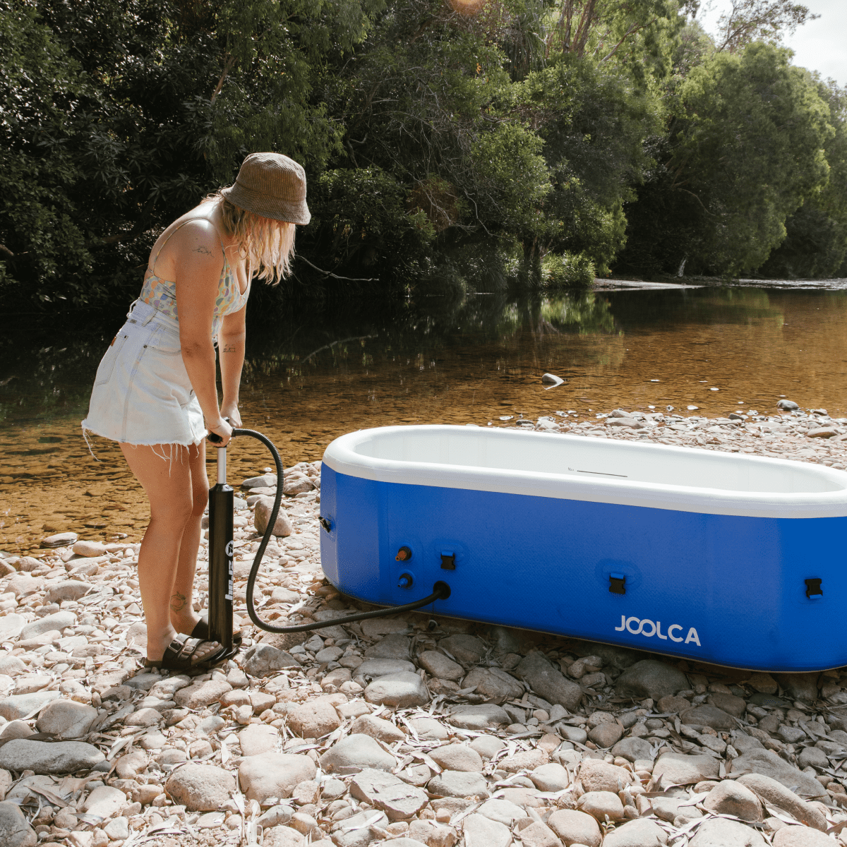 Woman inflating the Joolca HOTTUB with a hand pump on a riverbank