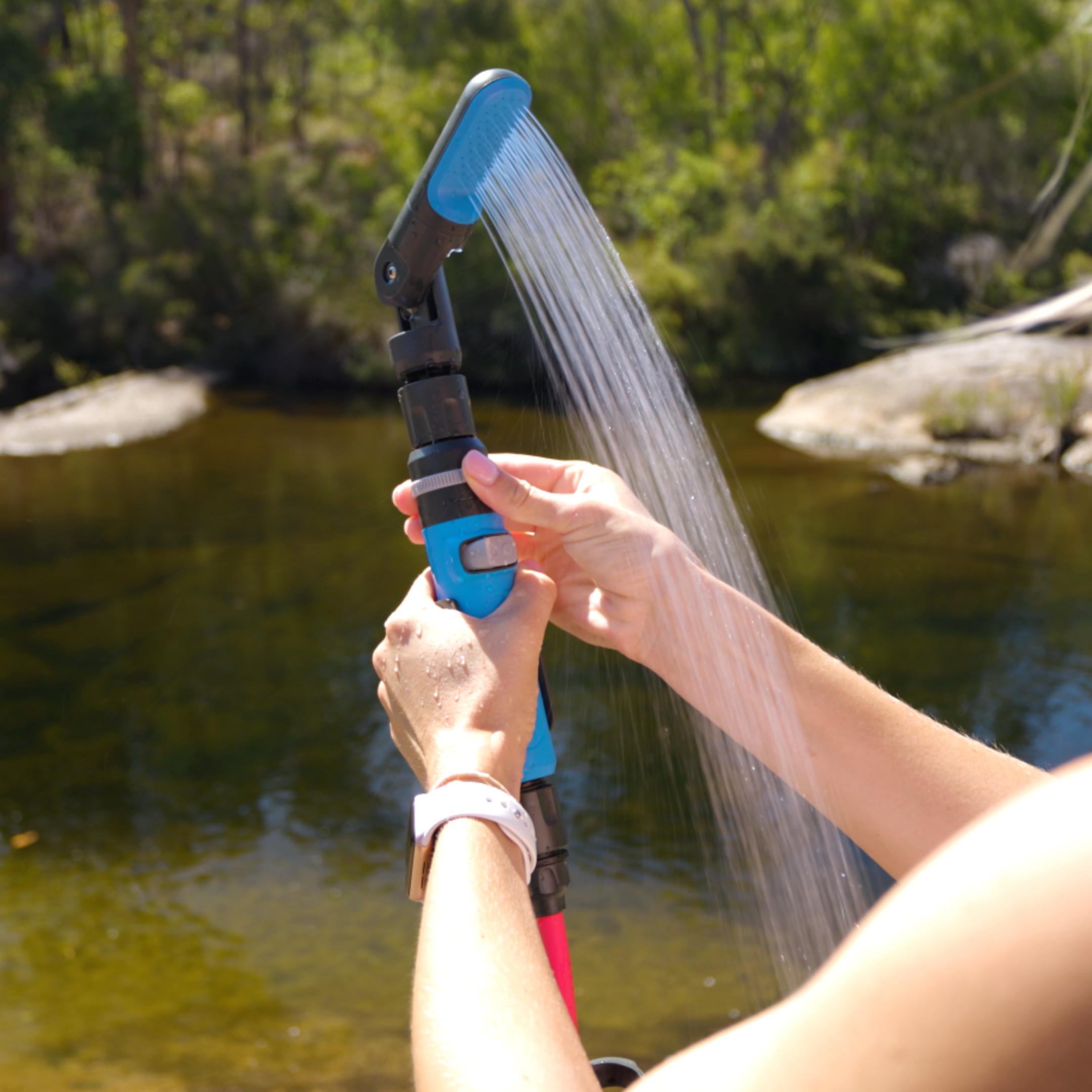 Hand holding the HOTTAP Go adjustable showerhead spraying water beside a river, angled at its pivoting joint