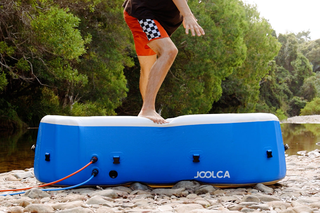 Person stepping barefoot onto the edge of an inflated HOTTUB on a rocky riverbank