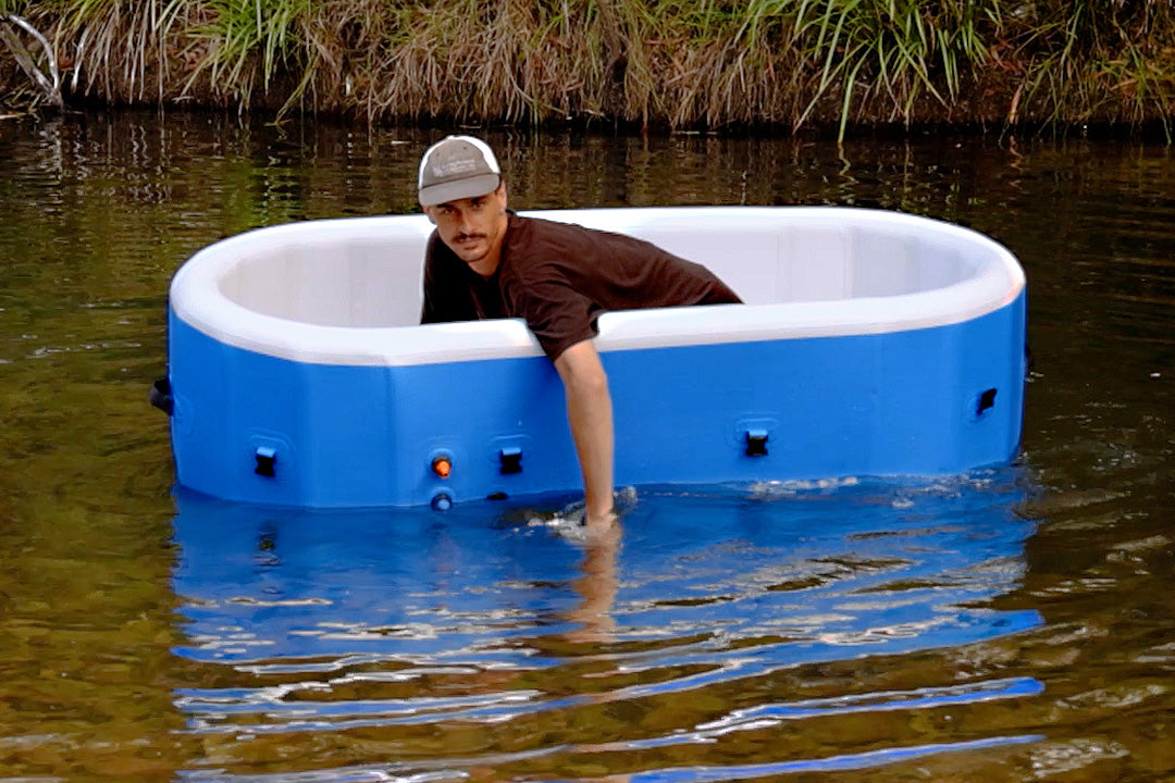 Man leaning into a HOTTUB set up in shallow water beside a grassy bank
